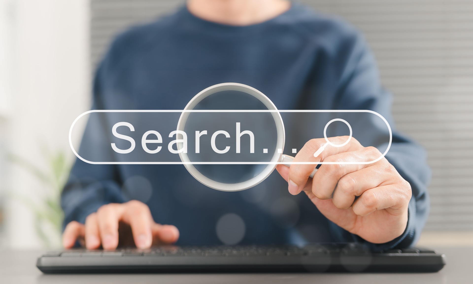 SEO search engine optimization concept. Person uses keyboard while holding magnifying glass with search bar labeled "Search", online search engine optimization, and digital marketing strategies.