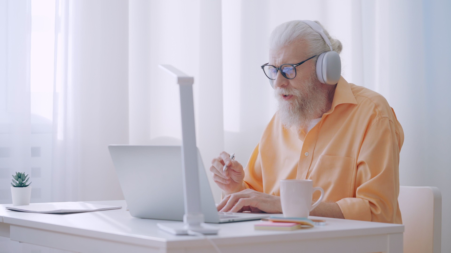 A man in his 60s works as an online tutor, having a video call and talking to coworkers